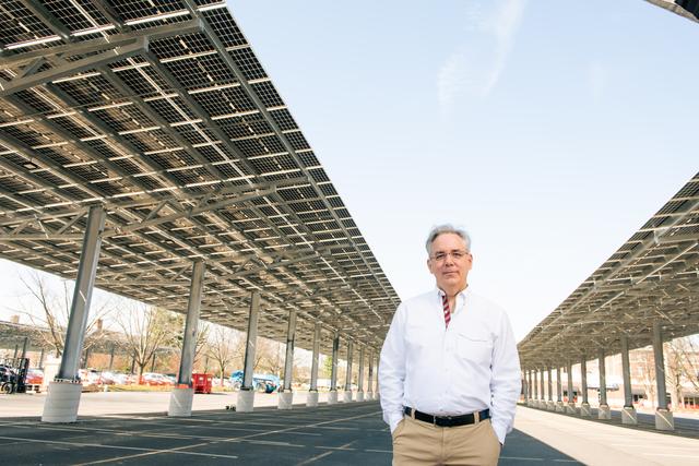 paul romano stands under solar array in TCNJ's parking lot