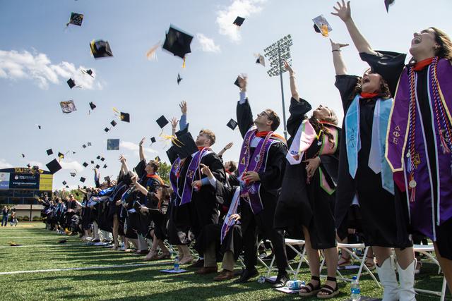 graduates toss their caps on the field in Lions stadium